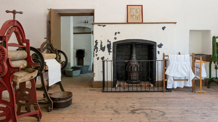 A fireplace in the laundry, surrounded by drying linens and clothes mangles.